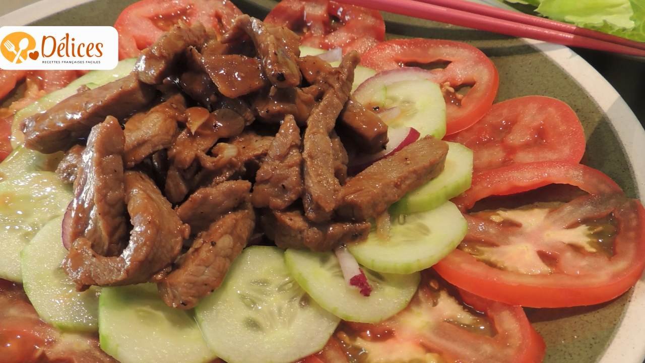 Gros plan sur un bol vert contenant des lamelles de bœuf sauté, des oignons, des concombres, des carottes et des feuilles de menthe.