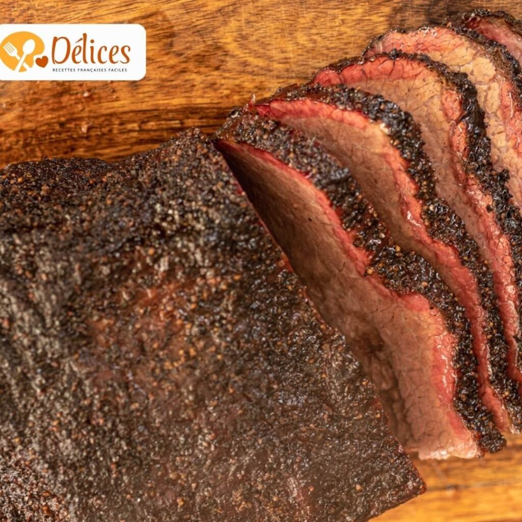 Gros plan sur un gros morceau de brisket de bœuf cuit et fumé, avec une croûte noire épaisse, coupé en tranches sur une planche en bois.