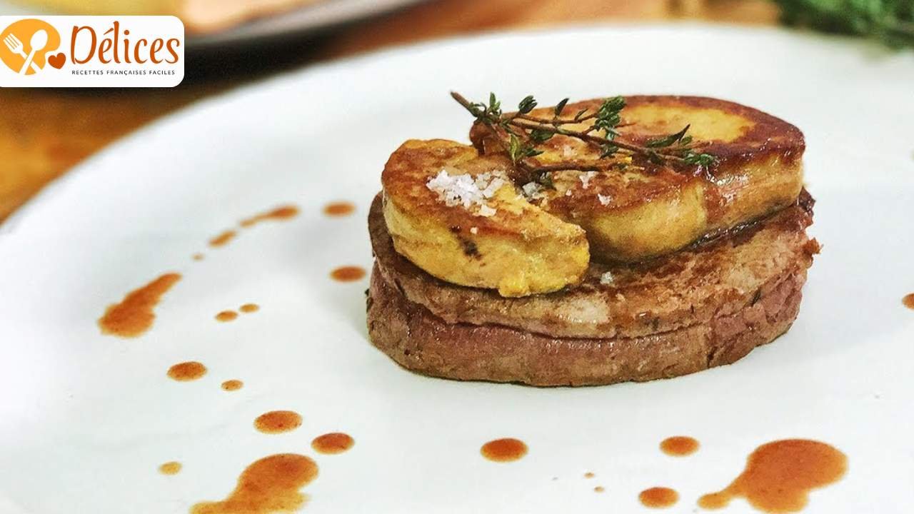 Gros plan sur un médaillon de filet de bœuf cuit et tranché, surmonté de deux tranches de foie gras poêlé et de thym frais sur une assiette blanche avec de la sauce. Image du filet de bœuf rossini.