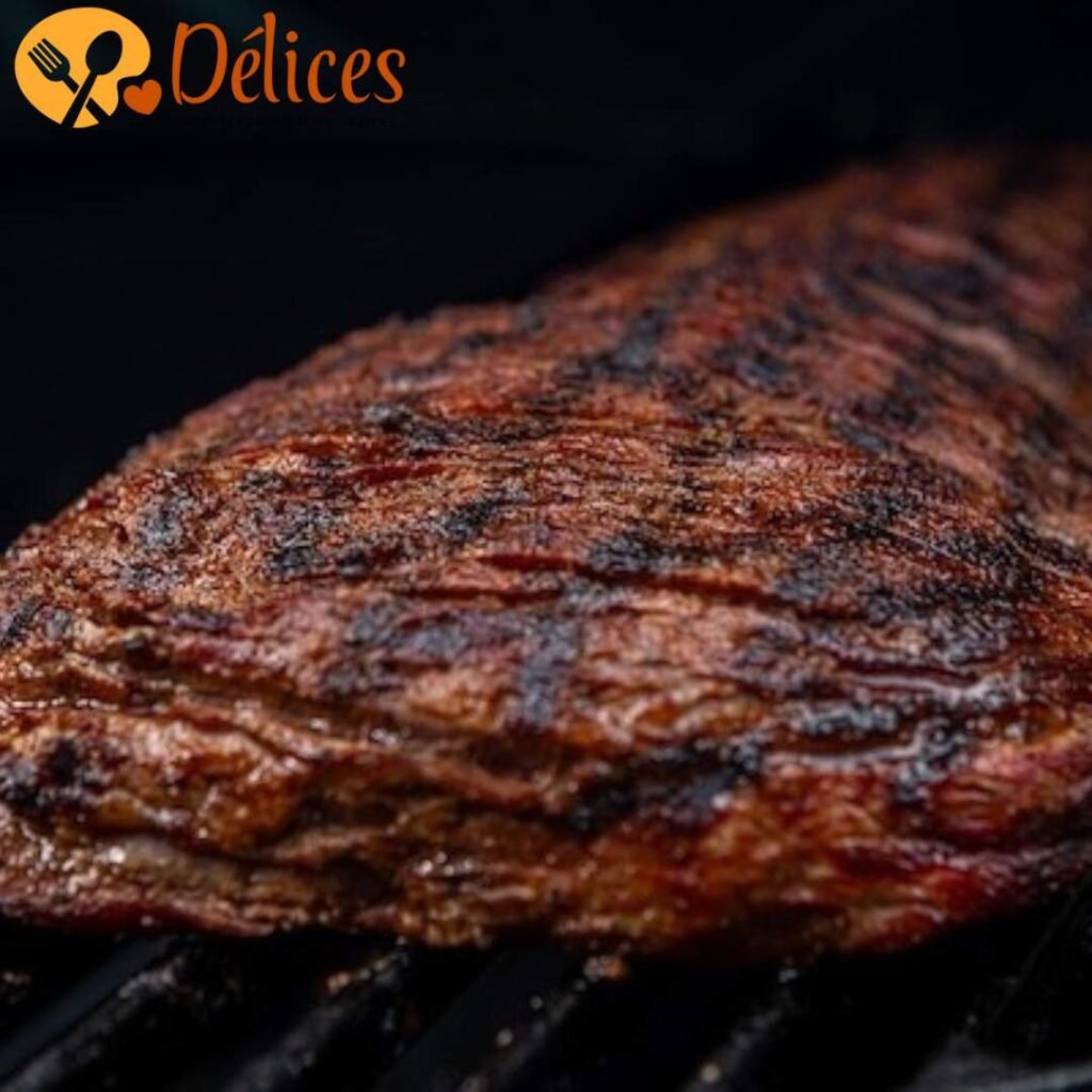 Gros plan sur une pièce de bavette de bœuf en train de griller sur un barbecue, montrant des marques de grillades foncées et la texture de la viande.