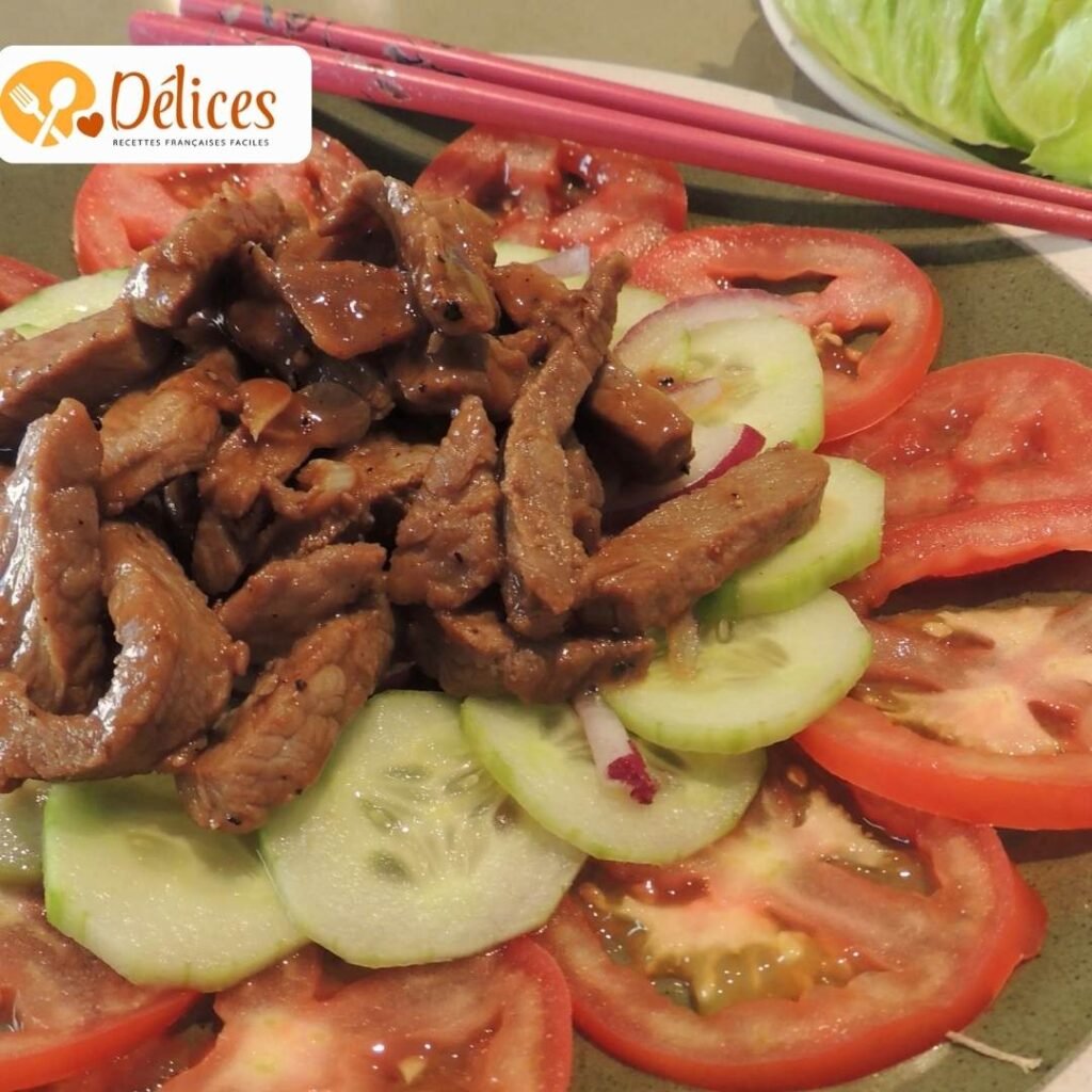 Gros plan sur des lamelles de bœuf sauté (Lok Lak) posées sur des tranches de concombres et de tomates, dans une assiette verte.
