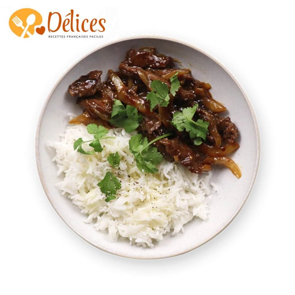Plat de bœuf aux oignons servi sur du riz blanc, garni de coriandre. Les lanières de bœuf sont nappées d'une sauce brune. Image de la Recette Bœuf aux Oignons.