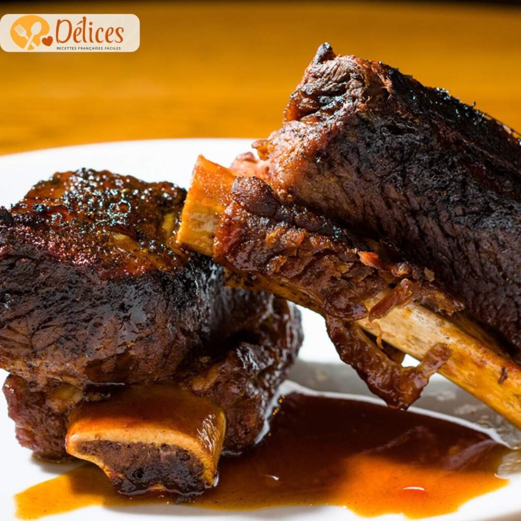 Gros plan sur deux morceaux de short ribs de bœuf braisés, l'os exposé, nappés d'une sauce brune épaisse et brillante, servis sur une assiette blanche. Image de la recette short ribs de boeuf fondants.
