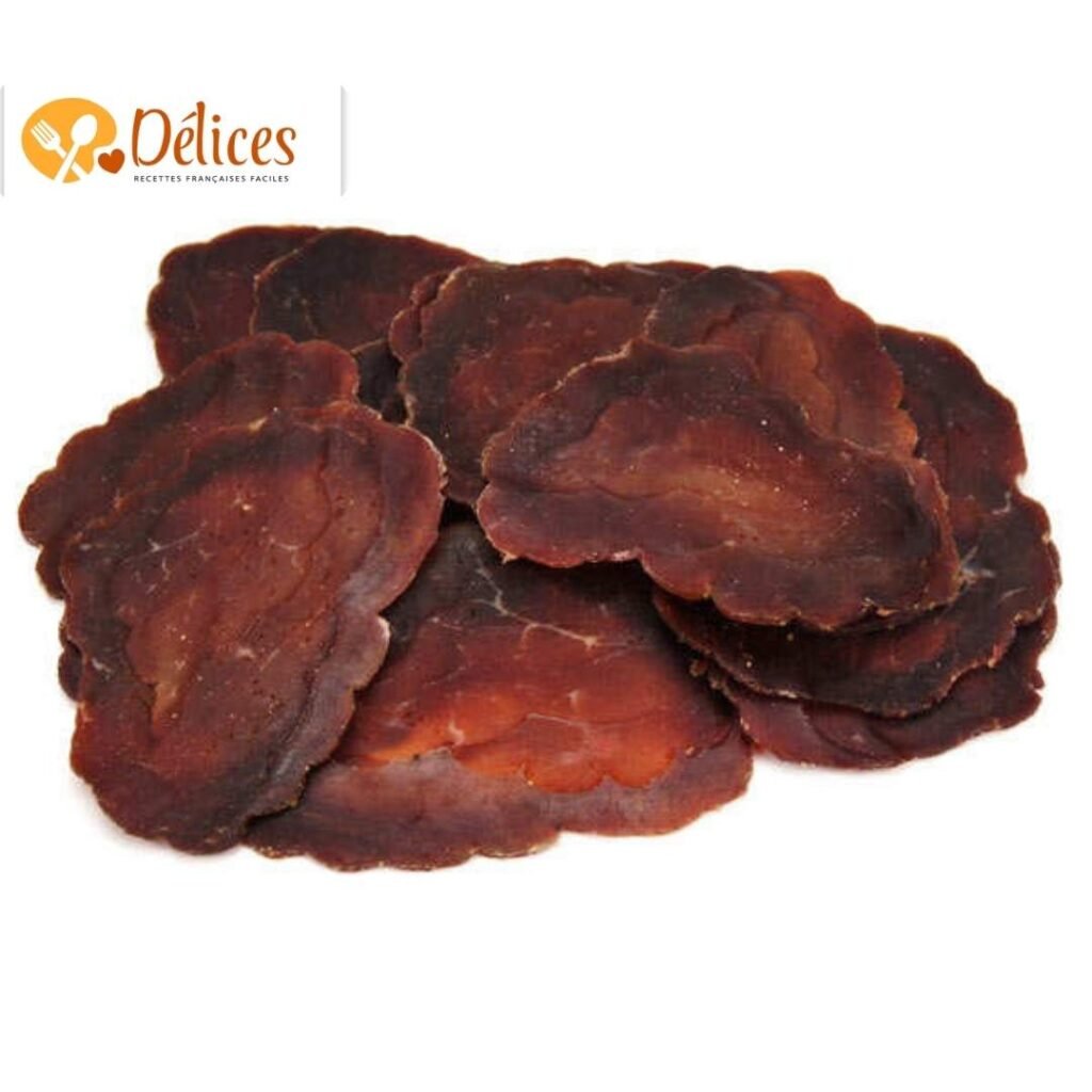 Gros plan de plusieurs fines tranches de Boeuf Seché artisanal sur fond blanc. Illustration de la texture ferme et de la couleur intense de la viande de boeuf seche.