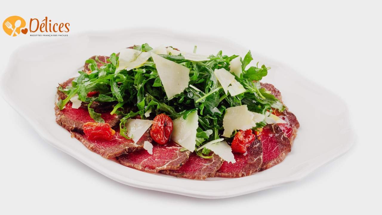 Gros plan d'une assiette de Carpaccio de Bœuf : fines tranches de bœuf cru recouvertes de roquette, de copeaux de parmesan et de tomates séchées.